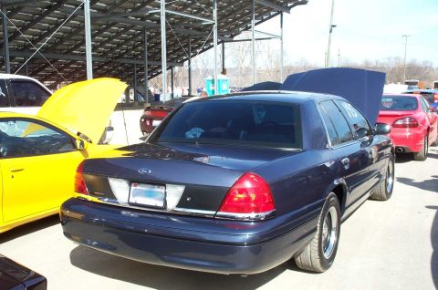 1998 Ford Crown Victoria - A dark blue sedan is parked at an outdoor event with other vehicles around it.