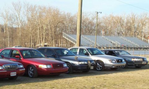 1998 Ford Crown Victoria - A line of Ford Crown Victorias are parked at what appears to be a racetrack.