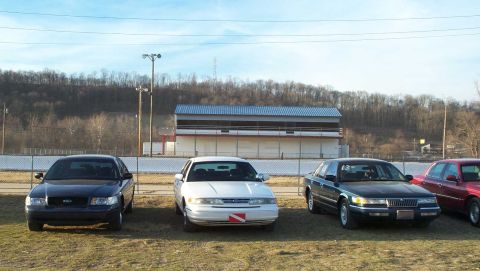 1998 Ford Crown Victoria - A lineup of sedans, including a 1998 Ford Crown Victoria, are parked outdoors near a building.