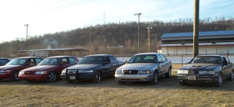1998 Ford Crown Victoria - Multiple Ford Crown Victoria sedans, including police interceptor models, are parked at Edgewater Raceway.