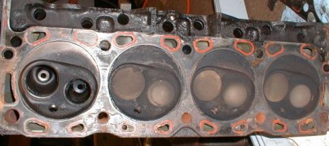 1990 Ford Bronco - Close-up of an engine cylinder head, revealing internal components and wear. The part is viewed from above, showing the combustion chambers.