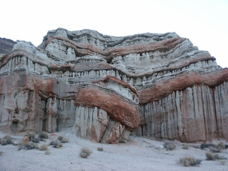 layered red and white rock formations with sparse desert brush
