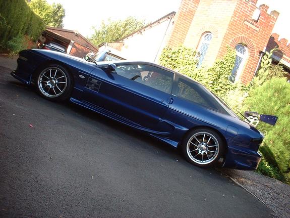 Blue 1995 Ford Probe with aftermarket wheels and a large rear spoiler parked on an asphalt driveway