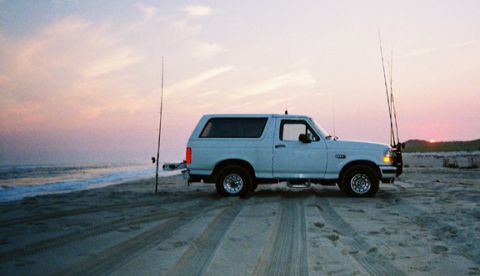 1996 Ford Bronco - Ford Bronco parked on the beach at sunset with fishing rods.