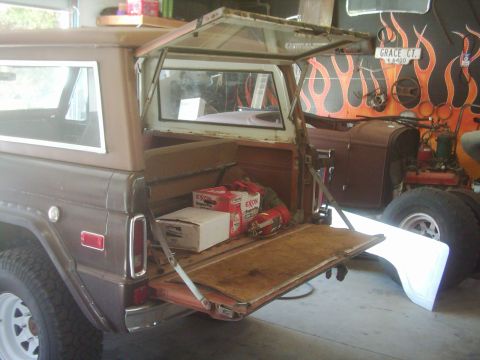 1978 Ford Bronco - The rear of a brown 1978 Ford Bronco is shown with its tailgate down, revealing cargo inside and another vehicle in the background.