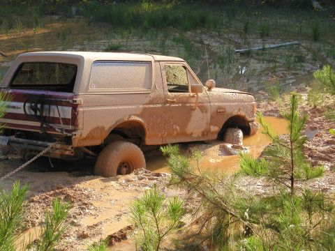 1989 Ford Bronco - This SUV is deeply stuck in the mud, with one wheel completely submerged in the muck.