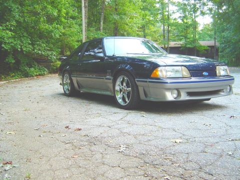 1989 Ford Mustang - 1989 Ford Mustang with custom wheels and two-tone paint sits on a cracked asphalt surface.