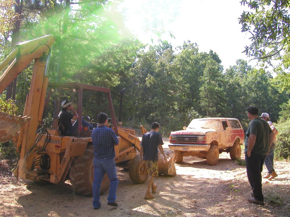 Muddy SUV and backhoe on a dirt road with trees around