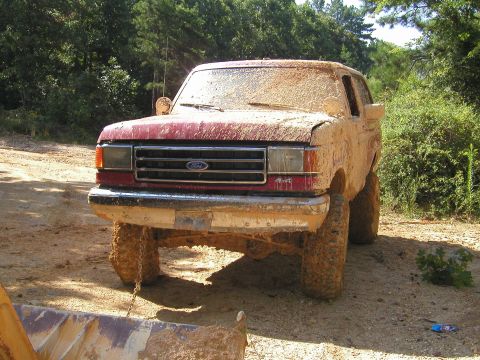 1989 Ford Bronco - This mud-caked 1987 Ford Bronco is seen from the front, its red paint barely visible beneath layers of dirt.
