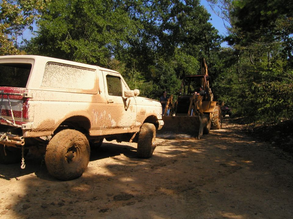 Mud-covered 1989 Ford Bronco parked next to a backhoe on a dirt road