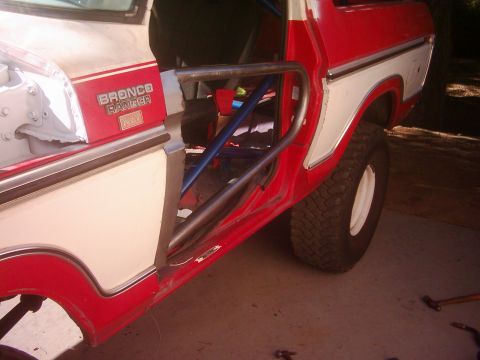 1978 Ford Bronco - The side of a red and white Bronco shows a "Bronco Ranger XLT" badge and a roll cage inside.