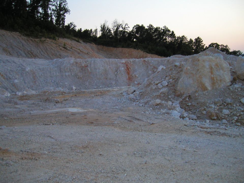 Quarry with dirt piles and trees under a dusky sky