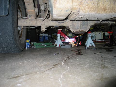 1995 Ford Bronco - The underside of a vehicle is supported by jack stands in a garage, revealing suspension components and a differential.