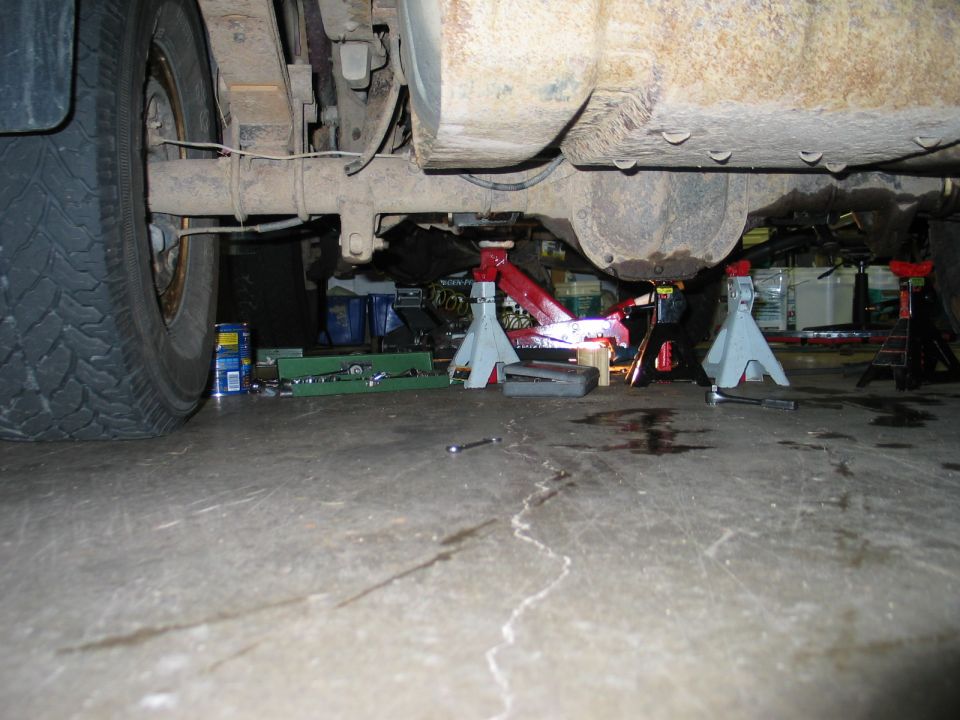 Undercarriage of a rusty vehicle on jack stands, showing suspension and differential