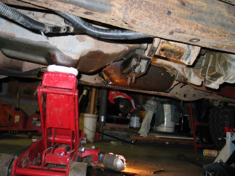 1995 Ford Bronco - Underside view of vehicle transmission and exhaust components, supported by a red jack in a garage setting.