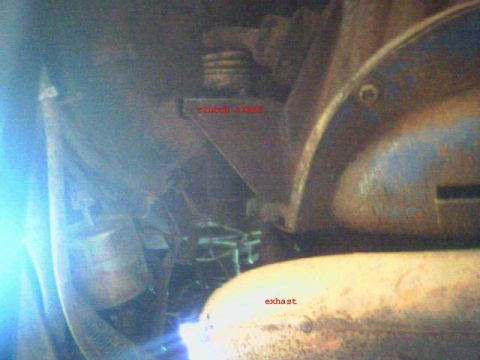 1987 Ford Bronco - Close-up view of vehicle undercarriage components, including exhaust and clutch linkage.
