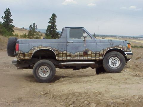 1989 Ford Bronco - A lifted first-generation-style Ford Bronco shown in side profile, with dark blue-gray paint featuring an airbrushed mountain/landscape mur…