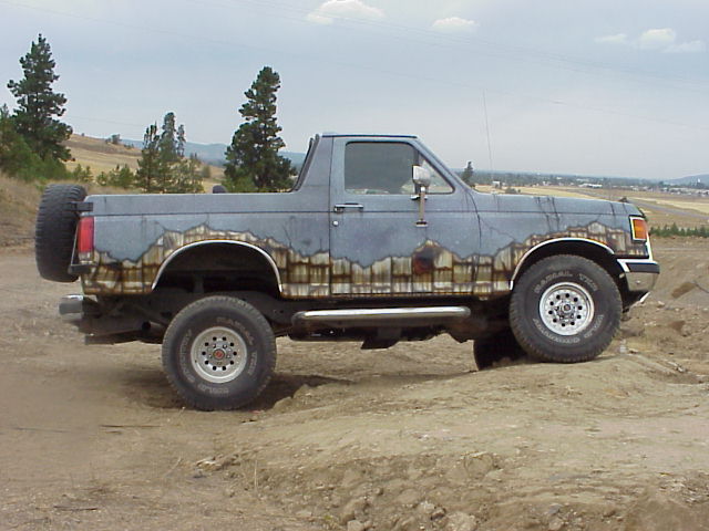 Lifted gray Ford Bronco with mountain mural, side view on dirt lot