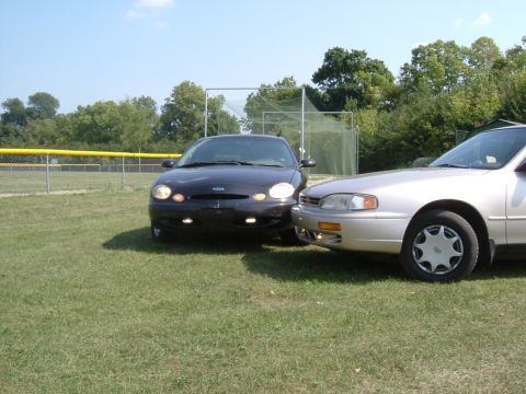 1996 Ford Taurus - A black 1996 Ford Taurus is parked on a grassy field next to another car.
