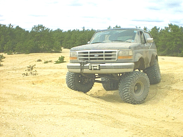 Lifted 90s Ford Bronco with tube bumper on mud tires parked in an open sand pit
