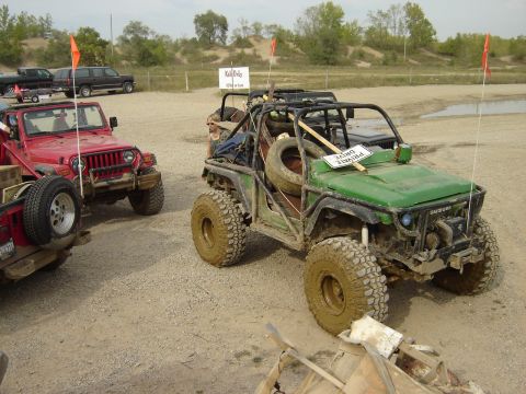 1992 Ford Bronco - Multiple off-road vehicles are parked on a dirt lot, with one green vehicle prominently in the foreground.