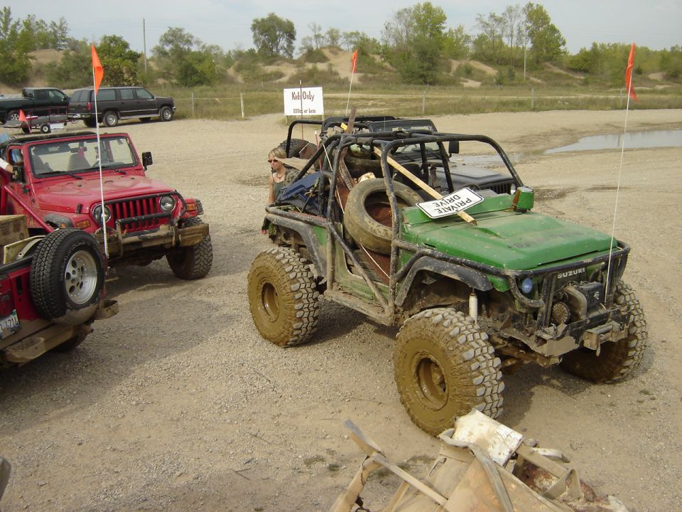 Green off-road vehicle with a roll cage, spare tire, and mud-covered tires