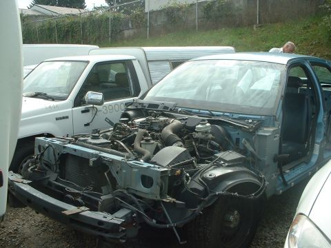 1999 Ford Crown Victoria - A light blue sedan with its front end removed, exposing the engine, sits next to a white pickup truck.