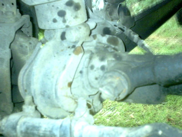 Underbody view of a vehicle's cast front differential, axle and driveshaft over grass