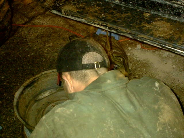 Man in work jacket kneeling over a bare steel wheel rim on a shop floor