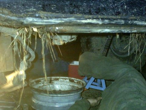 1995 Ford Bronco - Debris hangs from the undercarriage of a vehicle, with a wheel rim visible below.