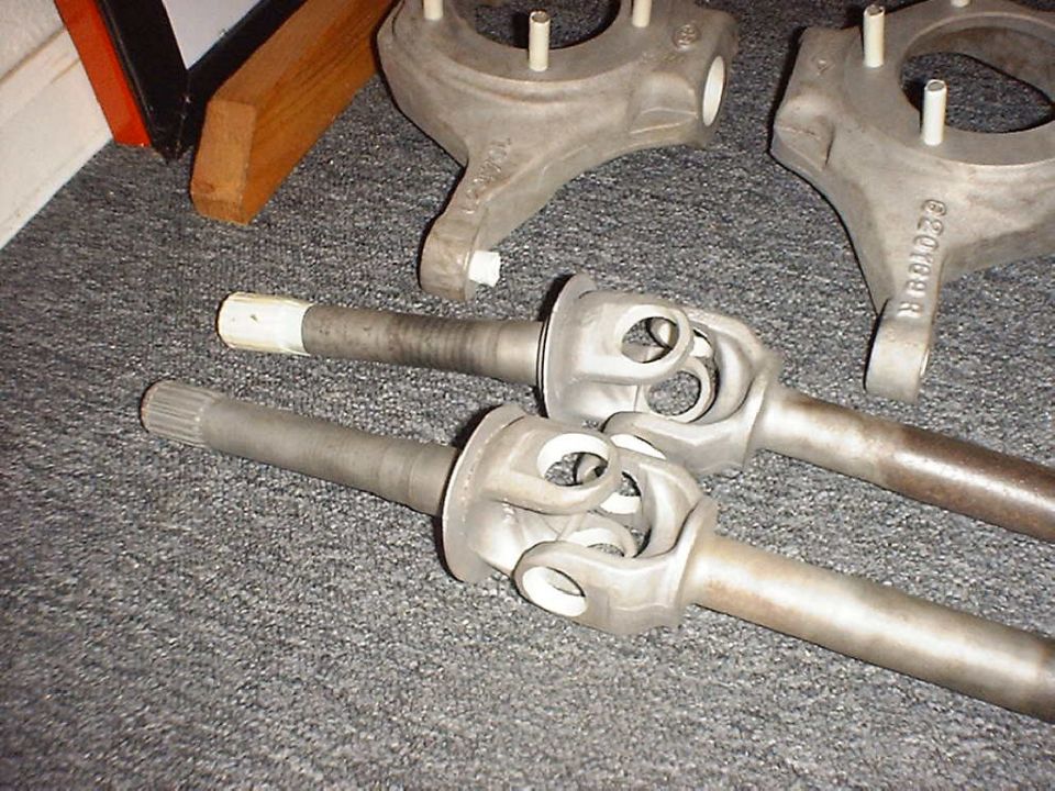 Two front axle shafts with U-joints and two steering knuckles laid out on gray carpet