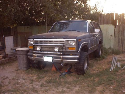 1988 Ford Bronco - This Ford Bronco, likely from the early 1980s, is parked in a yard with a brush guard and auxiliary lights on the front.