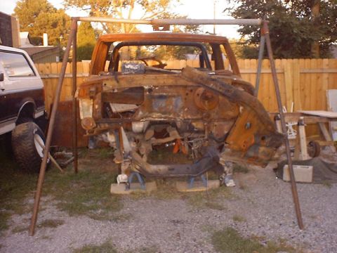 1988 Ford Bronco - Rusted vehicle chassis is supported by stands outdoors, with another vehicle partially visible.