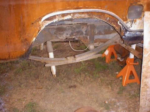 1988 Ford Bronco - The rear suspension and axle assembly of a vehicle, showing significant rust and supported by orange jack stands.