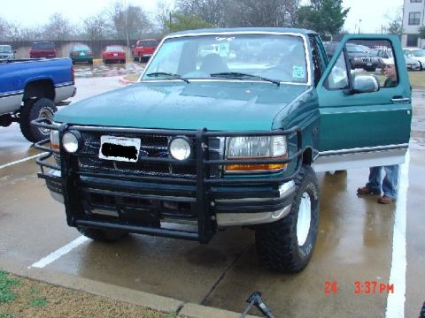 1995 Ford Bronco - A green 1995 Ford F-150 pickup truck is parked outside with its driver's door open.