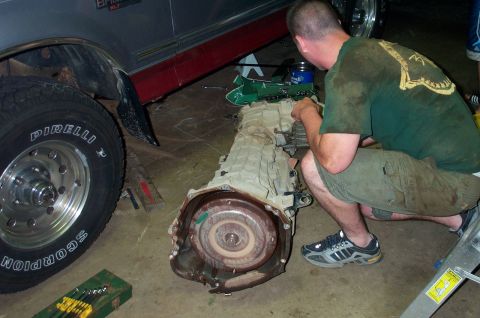 1995 Ford Bronco - Man working on a removed transmission next to a truck's wheel and fender.