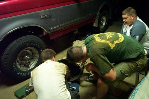 1995 Ford Bronco - Men work on the underside of a red and gray 1995 Ford Bronco in a garage.