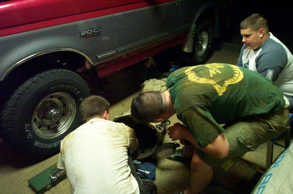Red and gray 1995 Ford Bronco side view with men working underneath