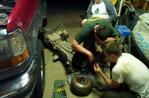 1995 Ford Bronco - Mechanics work on a transmission and torque converter, with a truck visible in the background.