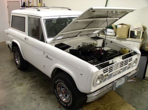 1967 Ford Bronco - A white 1966 Ford Bronco is parked indoors with its hood open, revealing the engine compartment.