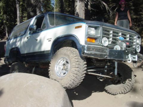 1986 Ford Bronco - Blue-and-white full-size Ford Bronco with 'BRONCO' fender lettering perched on granite rocks, viewed from the passenger-side front three-qu…
