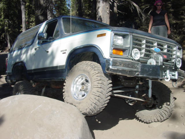 Blue and white Ford Bronco with winch flexed over granite rocks on mud-terrain tires