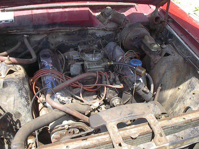 Dusty V8 engine bay of a red classic car with chrome carburetor and orange plug wires
