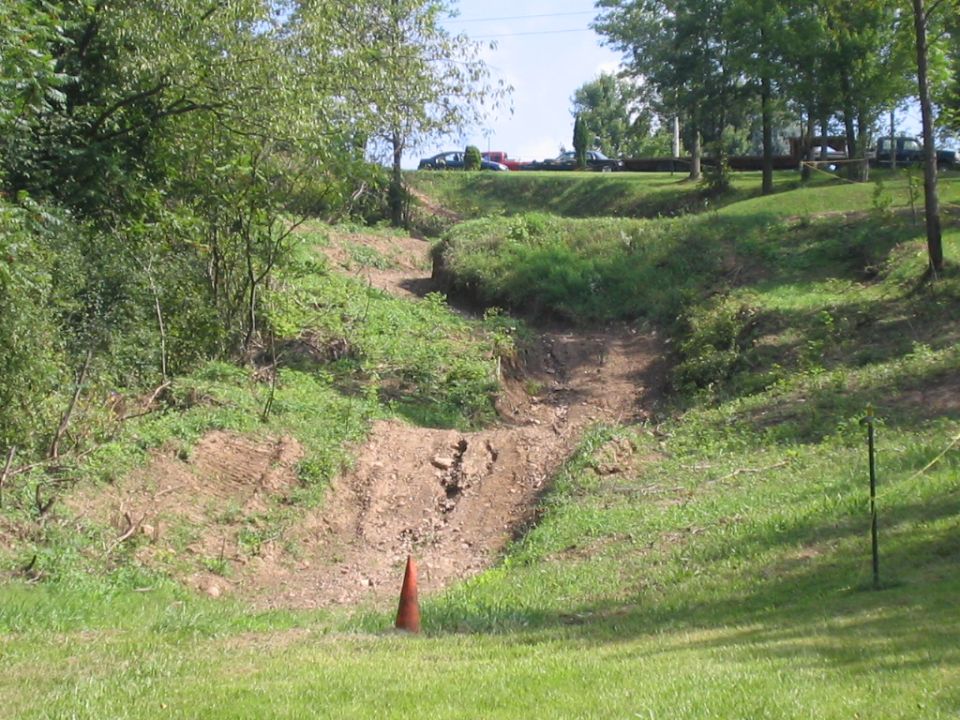 Eroded dirt hill-climb trail cut into a grassy slope with a single cone