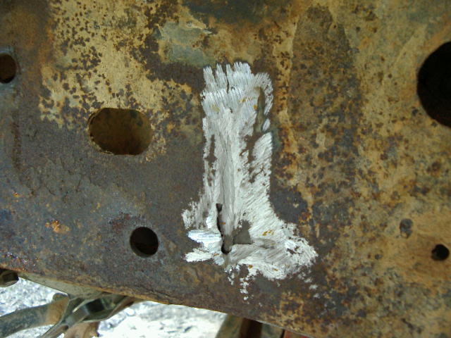 Rusty truck frame rail with a bracket ground off leaving bright bare-metal grinder marks