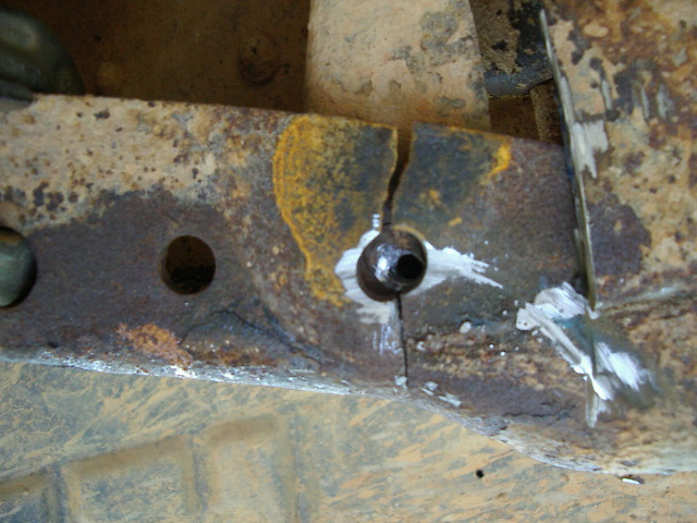 Cracked, rusted steel frame rail at a bolt hole marked with white chalk