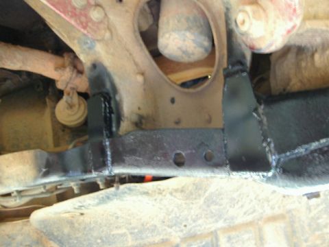 1985 Ford Bronco - Low underbody close-up of a newly fabricated black-painted crossmember welded between the frame rails, with two drilled holes in the flat f…