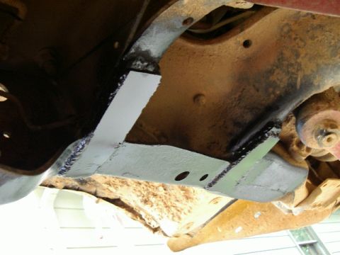 1985 Ford Bronco - Underbody view of a fabricated bare-steel crossmember freshly welded into the frame, with two drilled holes and dark weld beads along the j…