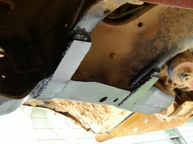 Bare steel fabricated crossmember welded into a dirty truck frame, seen from underneath