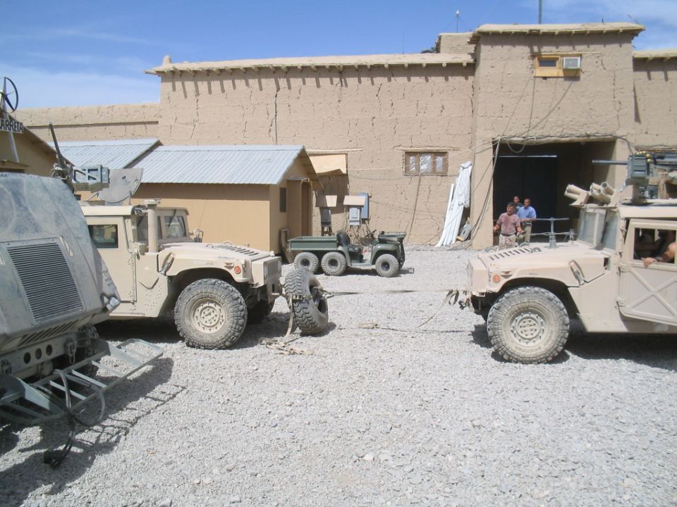 Military vehicles in a dusty compound, one being towed